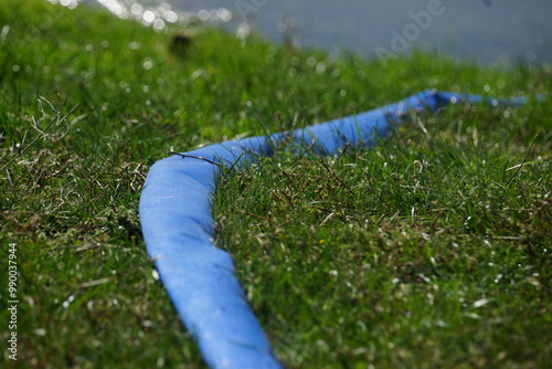 Macro of blue hose running along grassy field leading to pond, brightly lit