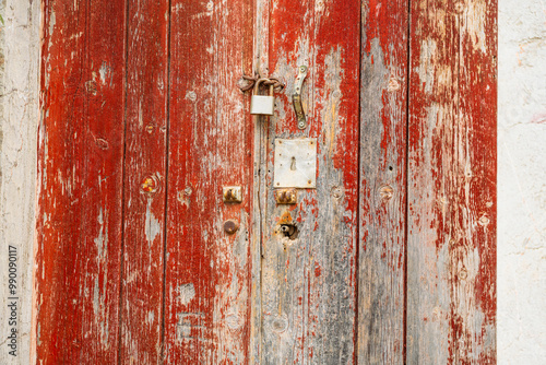 Abstract, Rustic, flaking, peeling red paint on a rotting and decaying door with rusty lock and keyhole at an abandoned house’s doorway