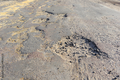 Bad road, cracked asphalt with potholes and big holes. Potholes on the road with stones on the asphalt. The asphalt surface is destroyed on the road. Bad condition of the road, needs repair.