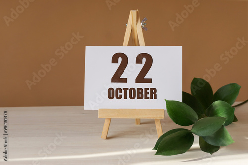 October 22th. Day 22 of month, Calendar date. Green branch, easel with the date and month on desktop. Close-up, brown background. Autumn month, day of year concept photo