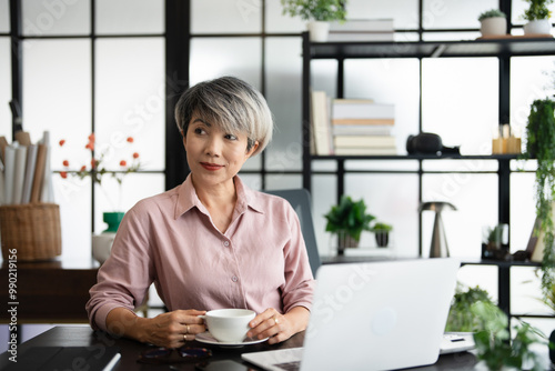 Successful businesswoman smiling holding coffee cup at office. Confident Asian business woman sitting and drinking coffee in the office.