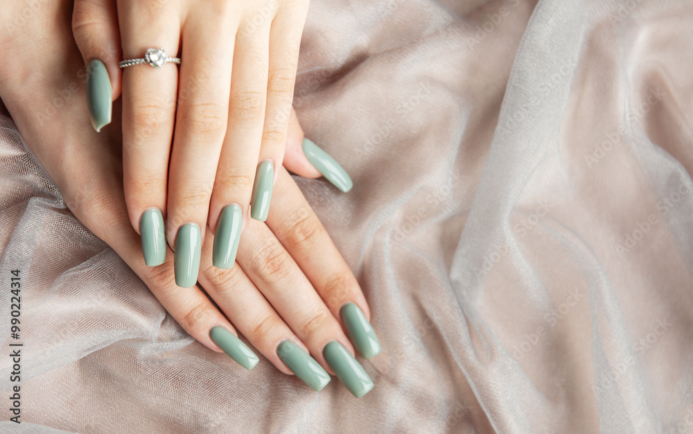Fototapeta premium Elegant hands with long green nails resting on soft fabric