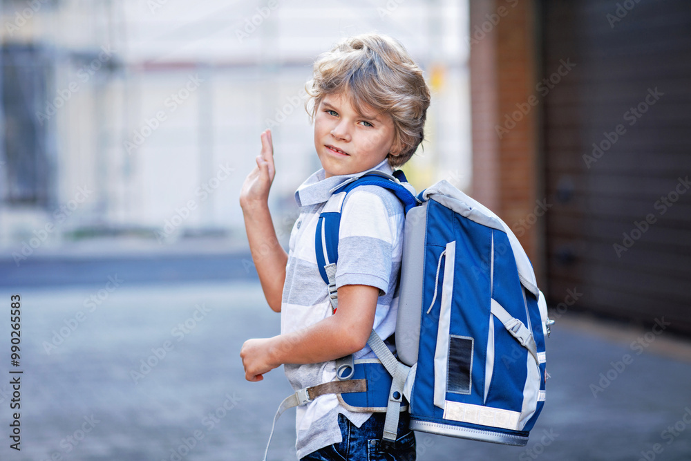 Fototapeta premium Happy little kid boy with satchel. Schoolkid on the way to school. Portrait of healthy adorable child outdoors. Student, pupil, back to school. Elementary school age