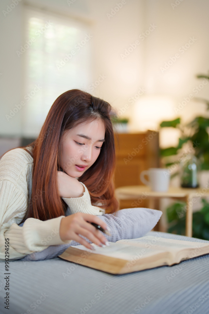 Young asian women in sweater lying on comfortable couch to enjoying with reading literature book and taking notes while relaxation and doing activity to spending time with slow life lifestyle at home. Young asian women in sweater lying on comfortable couch to enjoying with reading literature book and taking notes while relaxation and doing activity to spending time with slow life lifestyle at home.
