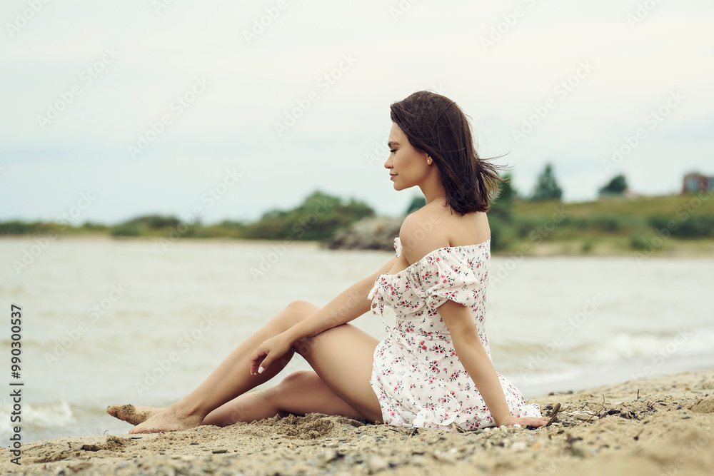 woman in a white dress is sitting on the beach by the sea, enjoying her rest and looking into the distance woman in a white dress is sitting on the beach by the sea, enjoying her rest and looking into the distance