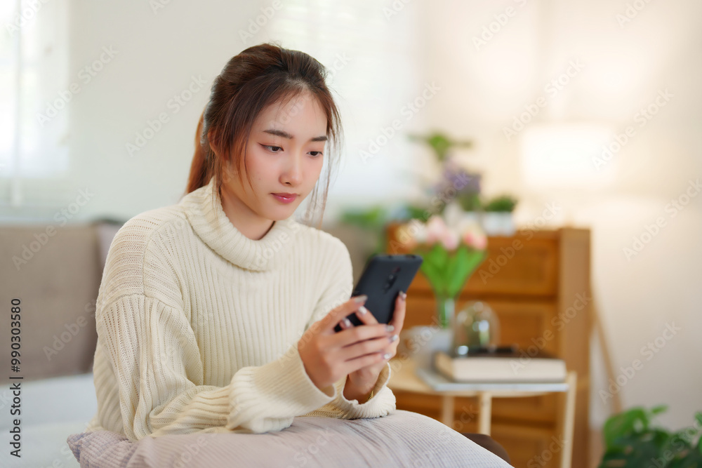 Young asian women in sweater enjoying with surfing entertainment on smartphone while sitting on comfortable couch to relaxation and doing activity for spending time with slow life lifestyle at home Young asian women in sweater enjoying with surfing entertainment on smartphone while sitting on comfortable couch to relaxation and doing activity for spending time with slow life lifestyle at home