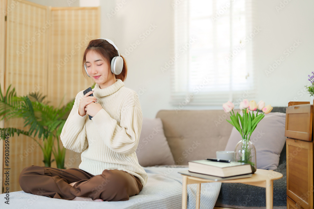 Young asian women in sweater wearing headphone to listening music and breathing while sitting on comfortable couch to relaxation and doing activity for spending time with slow life lifestyle at home Young asian women in sweater wearing headphone to listening music and breathing while sitting on comfortable couch to relaxation and doing activity for spending time with slow life lifestyle at home
