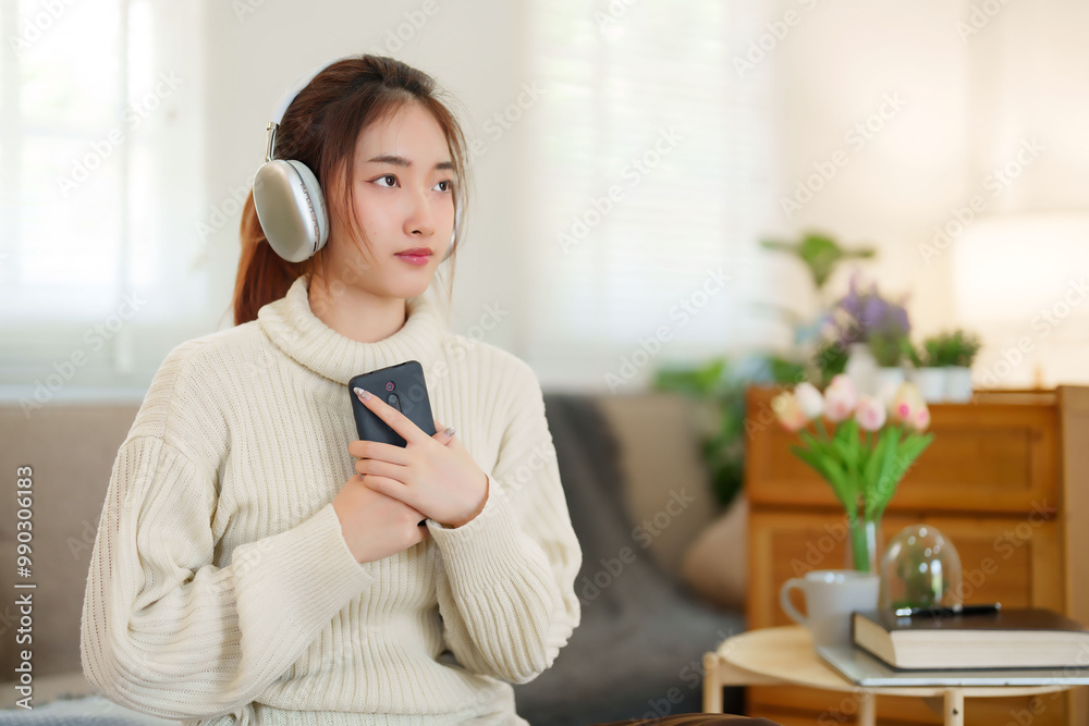 Young asian women in sweater holding smartphone and wearing headphone to listening the music with happiness while relaxation and doing activity for spending time with slow life lifestyle at home Young asian women in sweater holding smartphone and wearing headphone to listening the music with happiness while relaxation and doing activity for spending time with slow life lifestyle at home