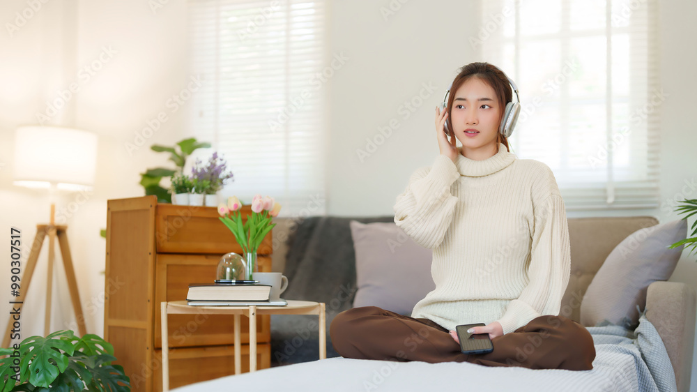 Young asian women in sweater wear headphone and listen music with enjoying on smartphone while sitting on the couch to relaxation and doing activity for spending time with slow life lifestyle at home Young asian women in sweater wear headphone and listen music with enjoying on smartphone while sitting on the couch to relaxation and doing activity for spending time with slow life lifestyle at home