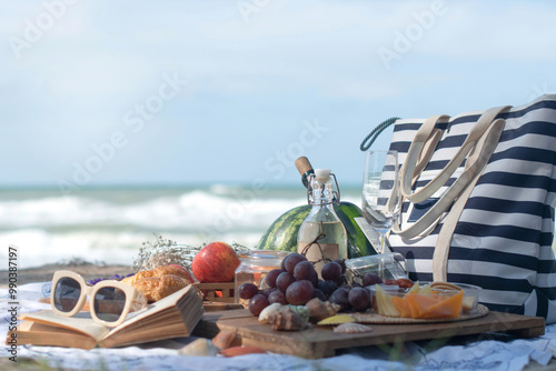 Picnic bag, food and drinks on a picnic cloth, outdoor picnic lunch with croissants, wine, fruits and cheese at the beach on a sunny day, sea waves in the background