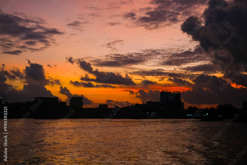 Sunset over Kapuas River in Pontianak, illuminating the sky with orange, pink, and purple hues, reflecting on calm waters. City skyline and mosque silhouette enhance the evening scenery.