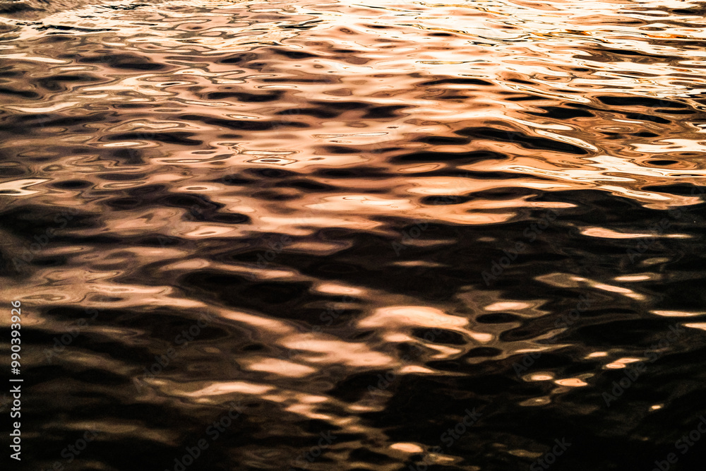 Golden reflections on rippling water create a mesmerizing texture with warm hues and dynamic patterns. Light and shadow interact, forming an abstract, tranquil, and calming natural scene.