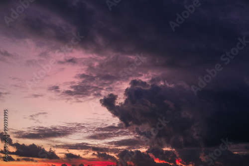 Obraz na płótnie Dramatic sunset sky with vibrant orange, pink, and purple hues blending into dark clouds over a city skyline, creating a stunning contrast between light and shadow in the evening atmosphere. w salonie
