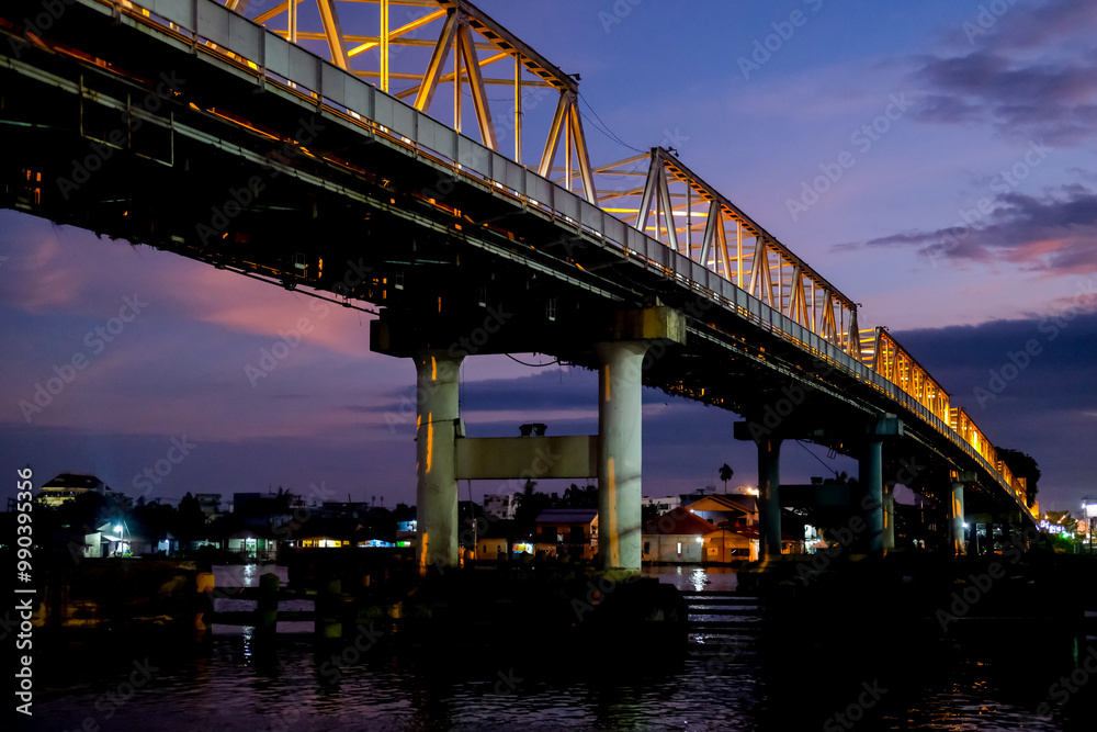 The Kapuas River Bridge in Pontianak glows beautifully at sunset, reflecting warm lights on the water. The scene captures the serene transition from day to night, showcasing urban charm. The Kapuas River Bridge in Pontianak glows beautifully at sunset, reflecting warm lights on the water. The scene captures the serene transition from day to night, showcasing urban charm.