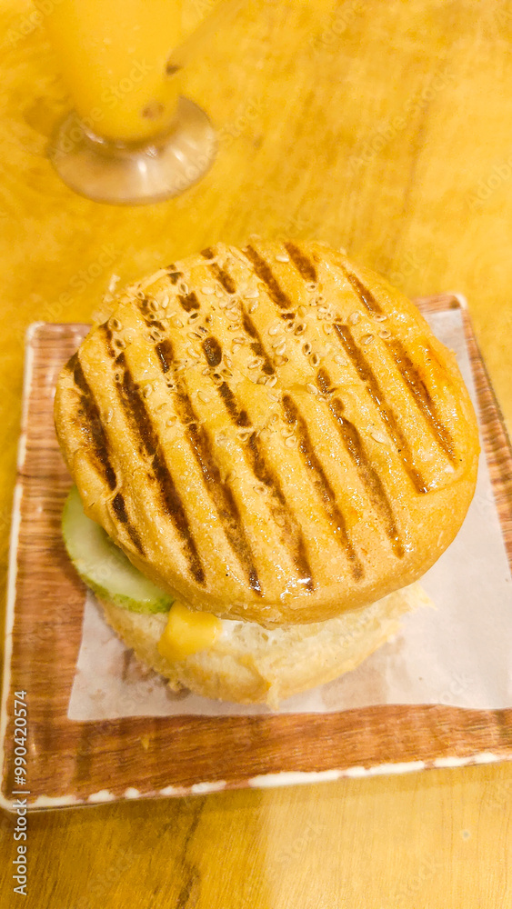Grilled chicken cheeseburger on a yellow table with juice beside it, all set on a wooden surface. A vibrant, appetizing food scene. Grilled chicken cheeseburger on a yellow table with juice beside it, all set on a wooden surface. A vibrant, appetizing food scene.