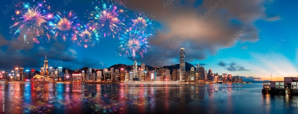 Fireworks explode over a vibrant Hong Kong cityscape, reflecting in the calm water. Fireworks explode over a vibrant Hong Kong cityscape, reflecting in the calm water.