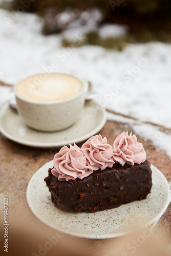 Aestetics vegan brownie witn no sugar cake dessert and cup of cappuccino outdoor at the snowy day. Coffee with dessert winter aesthetics. photo