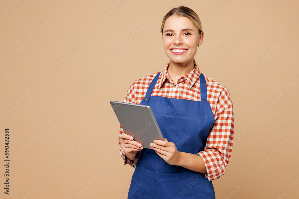 Obraz premium Young woman barista bartender barman employee wears blue apron red shirt work in coffee shop use digital tablet pc computer isolated on plain pastel beige background. Small business startup concept.