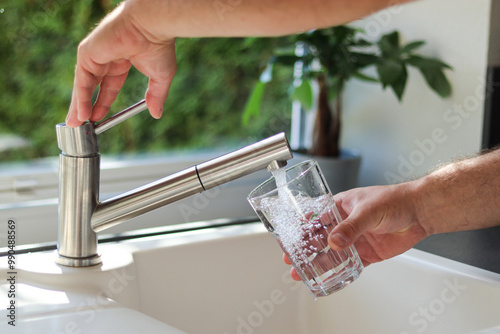 Close up of male hands pouring tap water into a glass in the kitchen photo