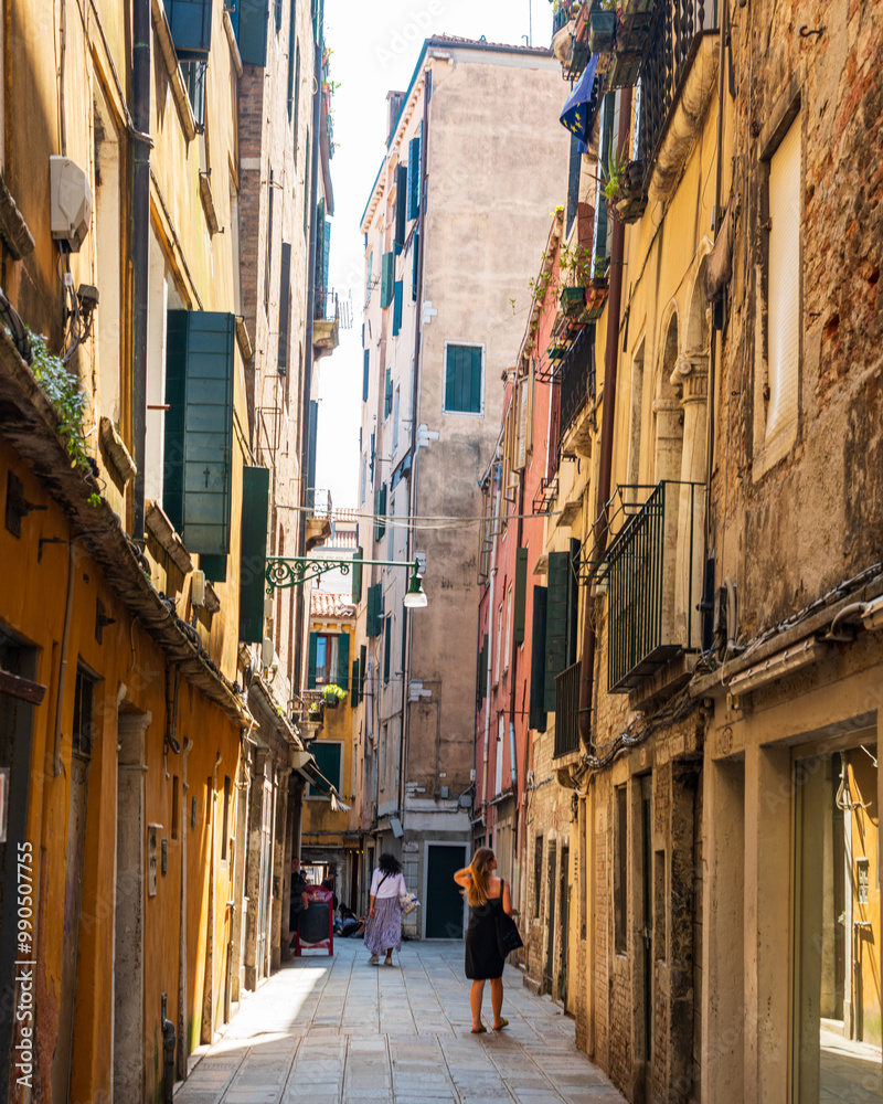Fototapeta premium petite ruelle dans le cœur du quartier San Marco à Venise, avec des maisons traditionnelles, et des venitiens qui se promènent en été.