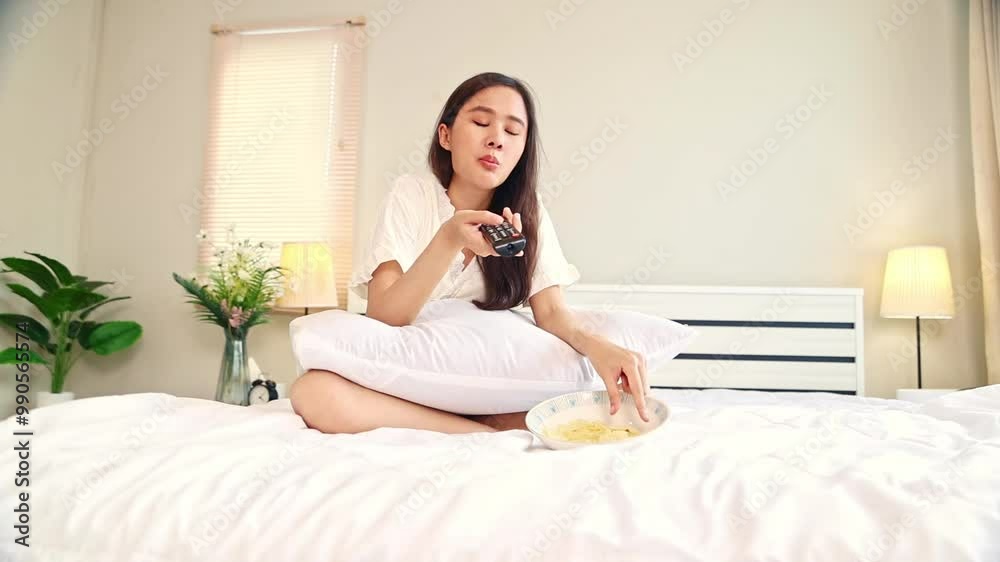 Happy woman eating snacks on the bed : Asian woman in pajamas watching TV and eating delicious potato chips snacks with hunger after waking up in the morning. Happy woman eating snacks on the bed : Asian woman in pajamas watching TV and eating delicious potato chips snacks with hunger after waking up in the morning.