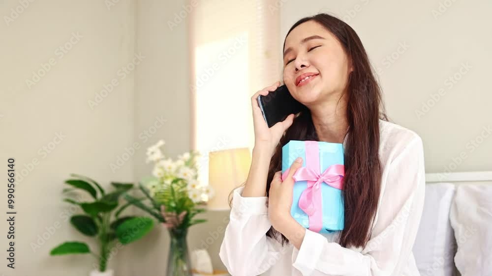 Portrait cute and happy young asian woman holding gift box tied with pink ribbon on her birthday anniversary given by her lover is calling thank her for the most wonderful gift with great emotion. Portrait cute and happy young asian woman holding gift box tied with pink ribbon on her birthday anniversary given by her lover is calling thank her for the most wonderful gift with great emotion.