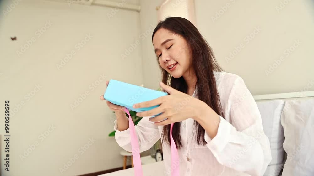 Most wonderful gift : Cute and happy asian woman holding gift box tied with pink ribbon shaking the gift box with curiosity on her birthday which she received from her lover. Most wonderful gift : Cute and happy asian woman holding gift box tied with pink ribbon shaking the gift box with curiosity on her birthday which she received from her lover.