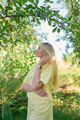 a portrait of a young blond girl in a yellow T-shirt and shorts among the trees on a summer day