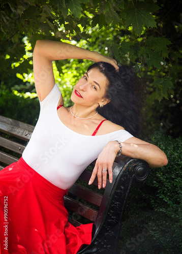 portrait of smiling brunette woman with curly hair sitting in the park in red skirt