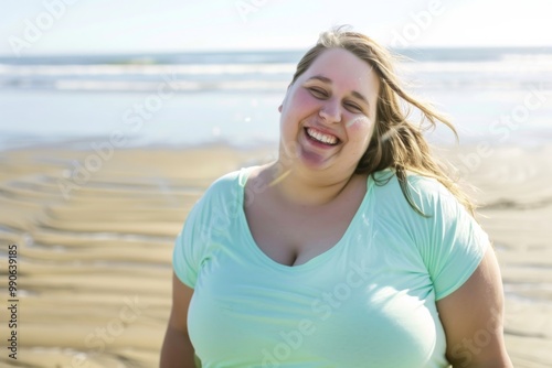 A young plus size woman radiates happiness with a bright smile as she stands by the beach, letting the ocean breeze play with her hair under the warm sun.