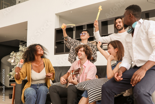 A group of multiracial teenagers is playing guitar and singing a song together while happily having fun blowing bubbles at the afternoon party. Recreational activity and celebration concepts.