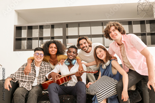 A group of multiracial teenagers playing guitar and singing a song together at an afternoon party. A group of Millennials sitting and spending time together on the holiday weekend..