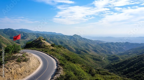 A winding road leads up a mountain to a red flag at the peak.