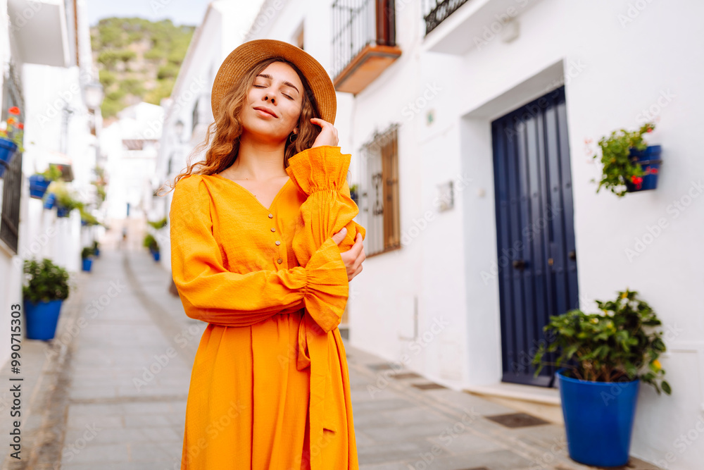 A young traveler woman in a vibrant orange dress and hat enjoys a sunny stroll through a charming white-washed village with flower pots. Concept of lifestyle, vacation, fashion, travel A young traveler woman in a vibrant orange dress and hat enjoys a sunny stroll through a charming white-washed village with flower pots. Concept of lifestyle, vacation, fashion, travel