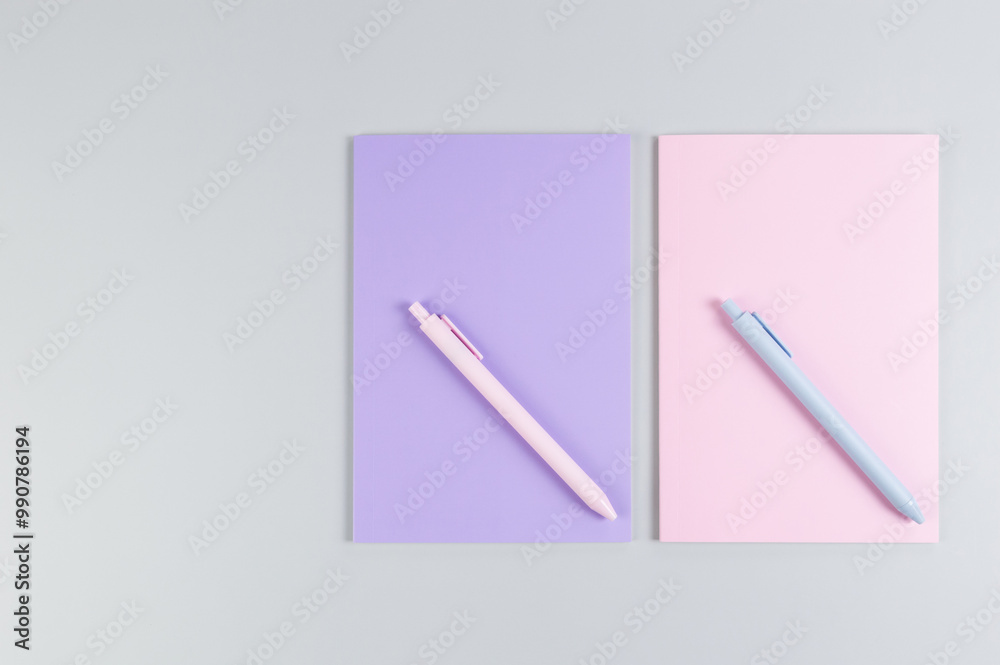Top view of pink and purple notebooks, pink and blue pens on grey background. School, office wallpaper. Flat lay, copy space.