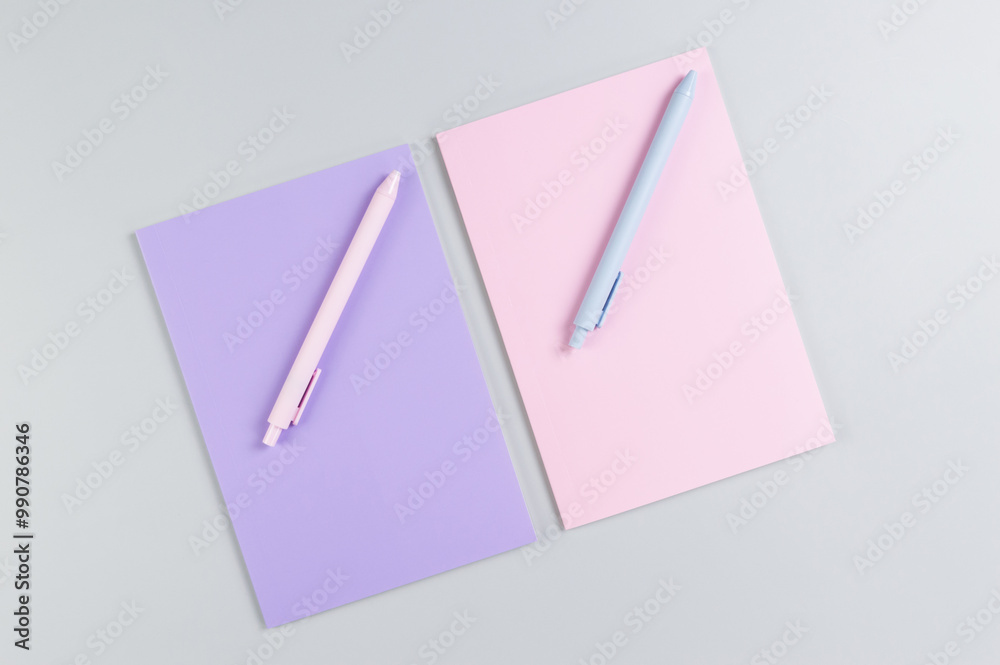 Top view of pink and purple notebooks, pink and blue pens on grey background. School, office wallpaper. Flat lay, copy space. Top view of pink and purple notebooks, pink and blue pens on grey background. School, office wallpaper. Flat lay, copy space.
