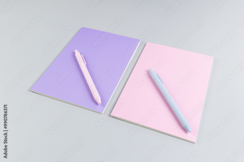 Top view of pink and purple notebooks, pink and blue pens on grey background. School, office wallpaper. Flat lay, copy space. Top view of pink and purple notebooks, pink and blue pens on grey background. School, office wallpaper. Flat lay, copy space.