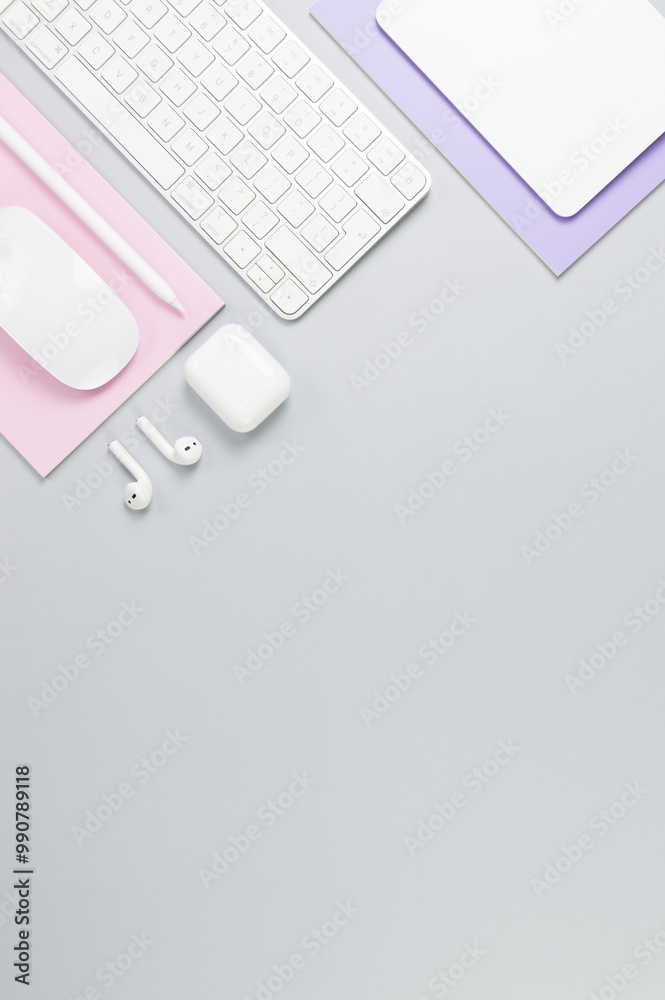 Top view of white keyboard, mouse, touchpad, earphones case, pen on grey background. Purple and pink notebooks, modern office, school. Flat lay, copy space.
