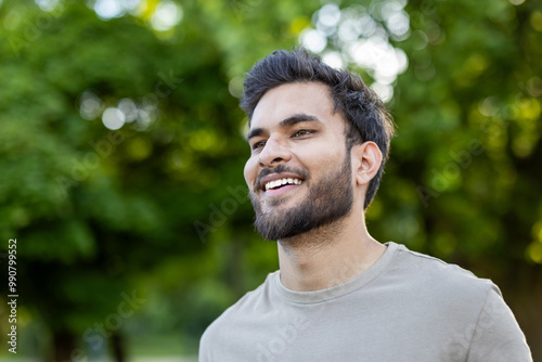 Close-up photo of a young Indian relaxed and happy young man who is in the park, walking, doing sports, smiling and looking away