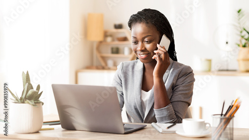 Millennial Black Businesslady Talking On Mobile Phone And Using Laptop At Workplace In Modern Office