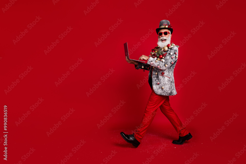 Full length photo of nice aged elegant man going hold laptop wear christmas tree balls costume sunglasses isolated red color background
