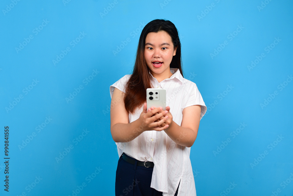 Surprised Asian woman looking at her smartphone over blue background with copyspace Surprised Asian woman looking at her smartphone over blue background with copyspace
