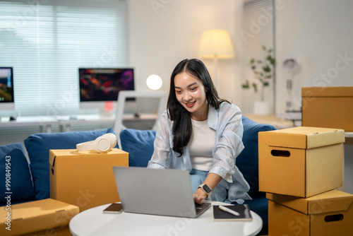 A woman is sitting on a couch in front of a laptop, smiling as she works