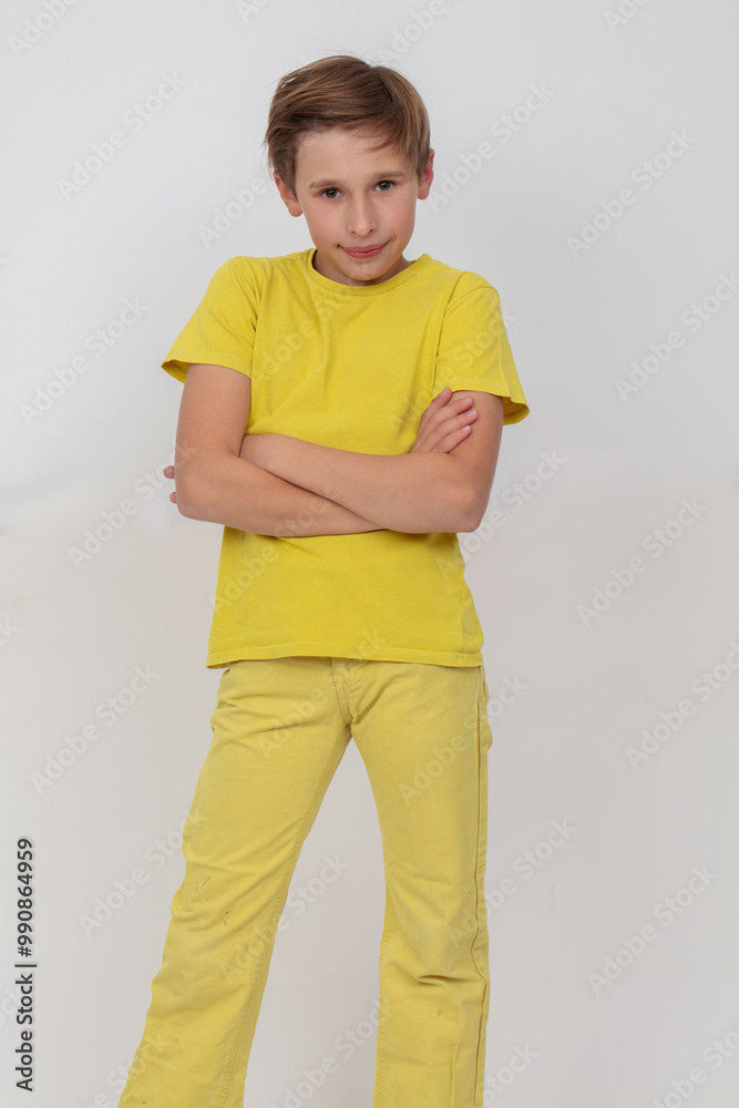 A young guy in a yellow shirt stands with his arms crossed and looks at the camera. He is in a serious or thoughtful mood.