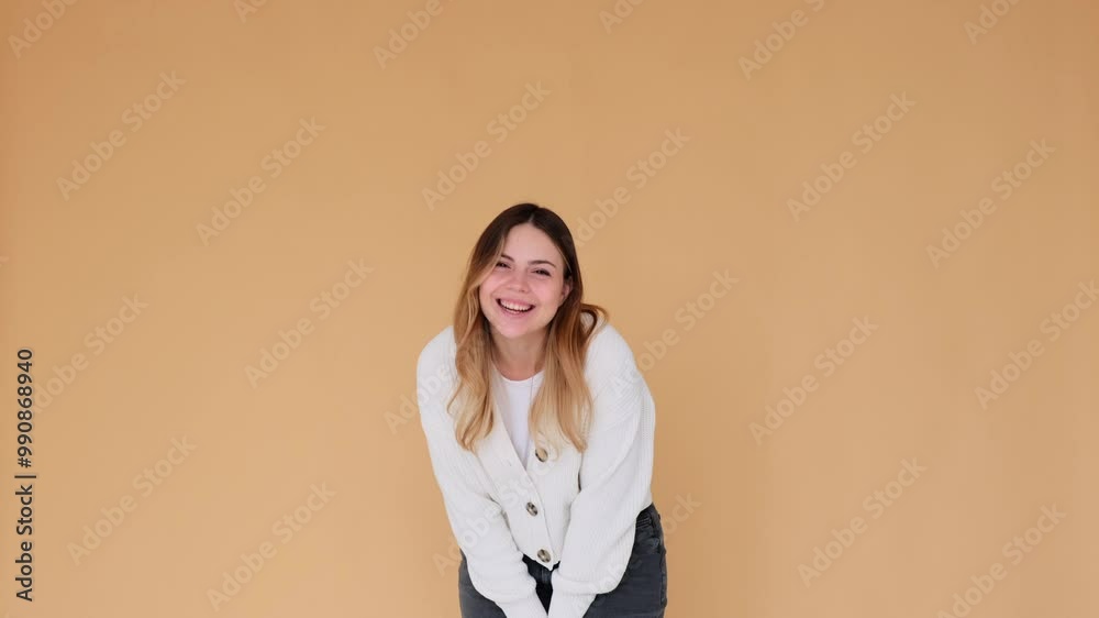 Happy and optimistic Caucasian young adult woman laughing and having playful mood, standing alone on beige background. Laughter, happiness, enjoyment concept. Happy and optimistic Caucasian young adult woman laughing and having playful mood, standing alone on beige background. Laughter, happiness, enjoyment concept.