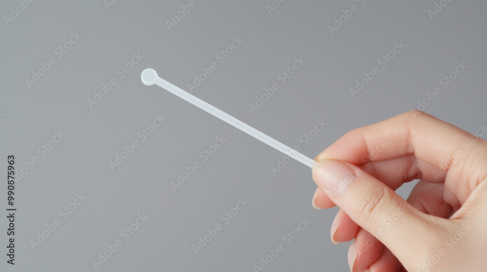 A hand holding a thin, white swab with a small round tip against a gray background. A hand holding a thin, white swab with a small round tip against a gray background.