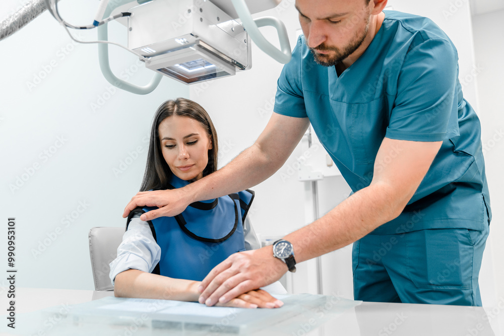 Obraz premium Male doctor works with an x-ray machine in a modern hospital while patient sitting on special sit. Radiologist takes a picture of the arm. The concept of medical technologies, modern medical equipment