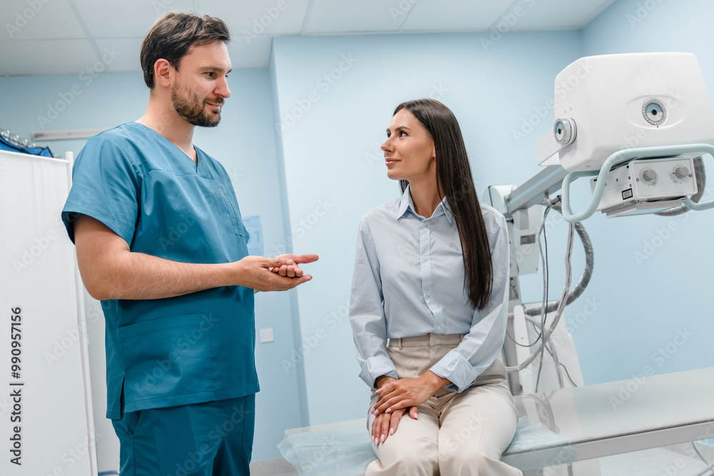 Medical worker specialist is talking to patient. Male radiologist is standing near patient woman and explaining X-ray procedure. Female patient is smiling and listening to doctor carefully. Medical worker specialist is talking to patient. Male radiologist is standing near patient woman and explaining X-ray procedure. Female patient is smiling and listening to doctor carefully.