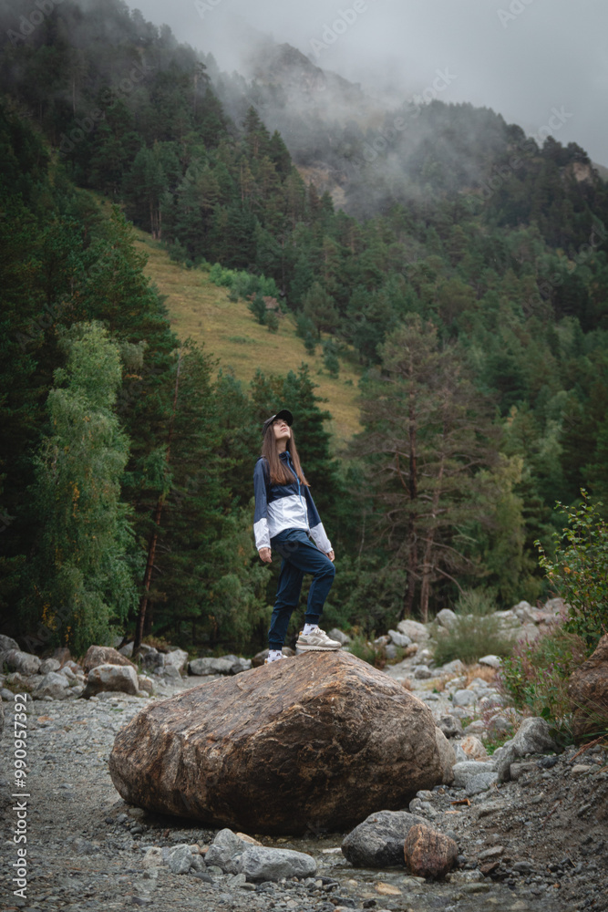 A girl in the mountains in the forest stands on rocks in blue sportswear panorama A girl in the mountains in the forest stands on rocks in blue sportswear panorama