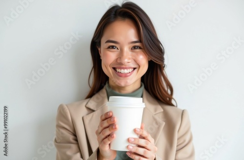 A young girl stands with a paper cup for takeaway coffee drinks or tea on a white background. Place for text